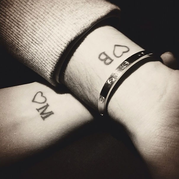 Matching couple tattoos on wrists with initials and hearts, symbolizing eternal love.