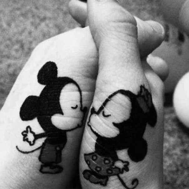 Matching couple tattoos of cartoon mice kissing on wrists.