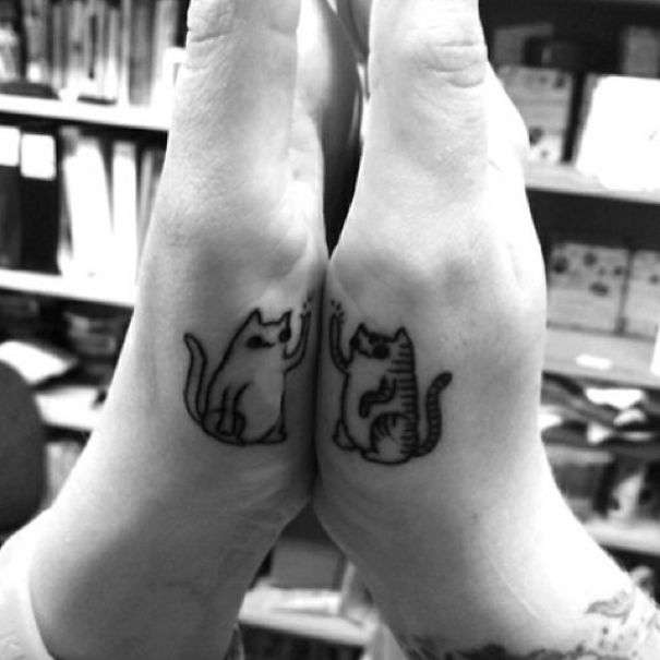 Matching couple tattoos of two cats high-fiving on hands.