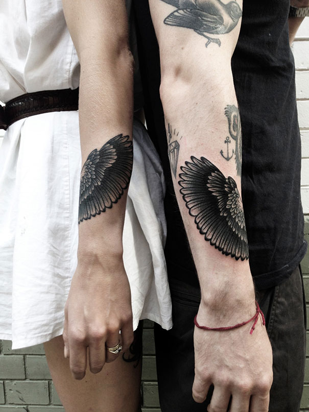 Matching couple tattoos on arms show detailed black wings.
