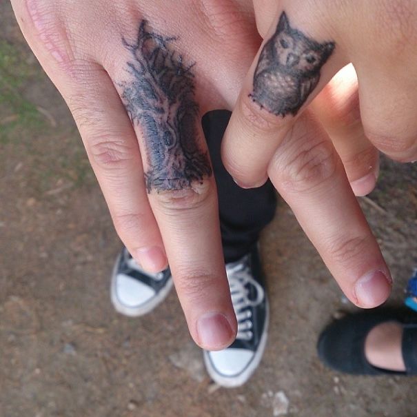 Matching couple tattoos on fingers, featuring a tree and an owl design.