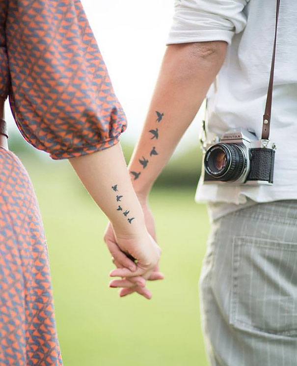 Couple holding hands with matching bird tattoos, symbolizing lasting love.