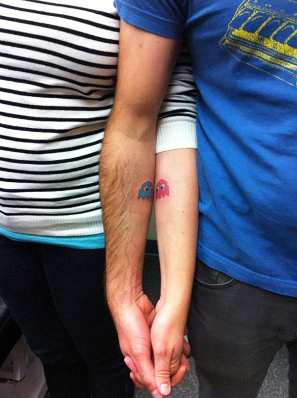 Matching couple tattoos featuring Pac-Man ghosts on arms of a couple holding hands, symbolizing love and connection.