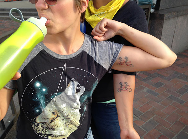 Couple showing matching bicycle tattoos on arms, symbolizing love and commitment.
