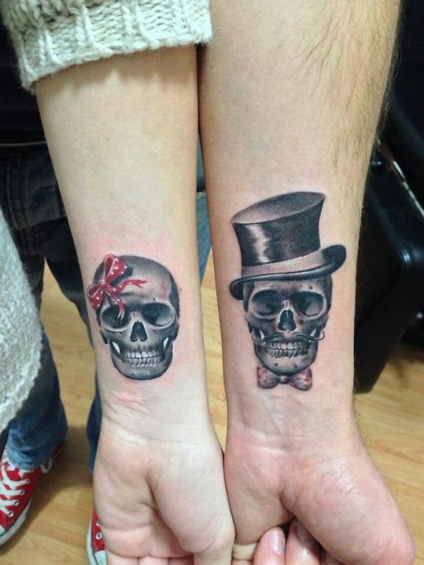 Matching couple tattoos of skulls with a bow and top hat on forearms.