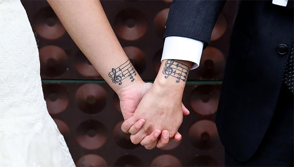 Couple holding hands with matching music note tattoos, symbolizing their love and commitment.