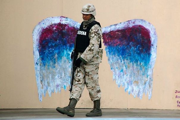 A Soldier Walks Past Graffiti Depicting Angel Wings