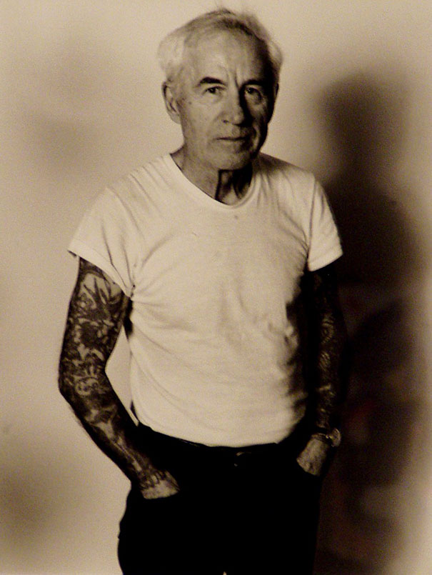 Senior man with tattooed arms in a white t-shirt, highlighting how ink looks on aged skin.