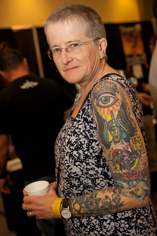 Senior with detailed arm tattoos in a patterned dress at an event, showcasing aging ink in vivid colors.