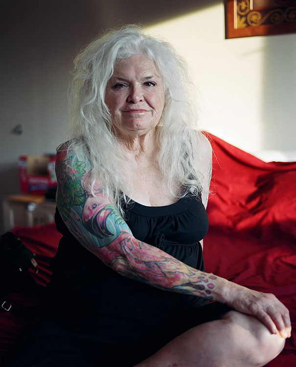 Senior woman with tattoos sitting on a bed, showcasing how ink appears at 60.