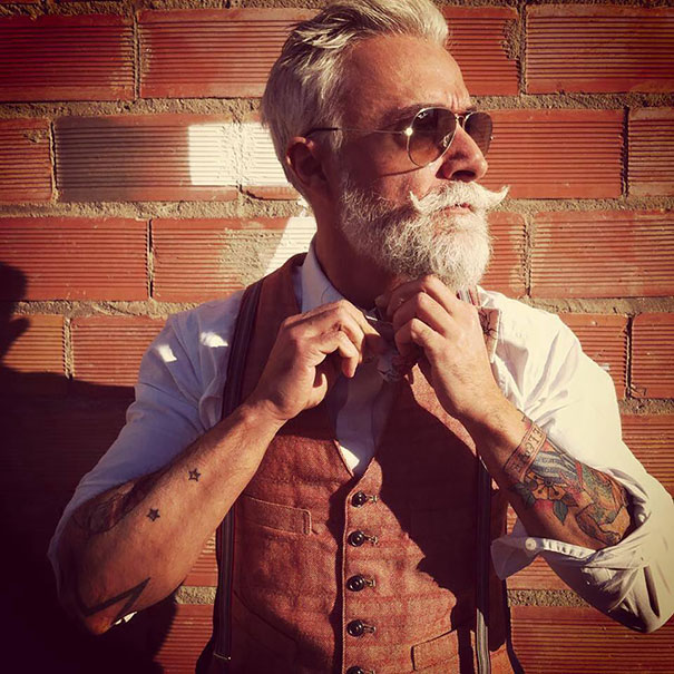 Senior with tattoos and sunglasses adjusts bow tie, showcasing how ink looks at 60.