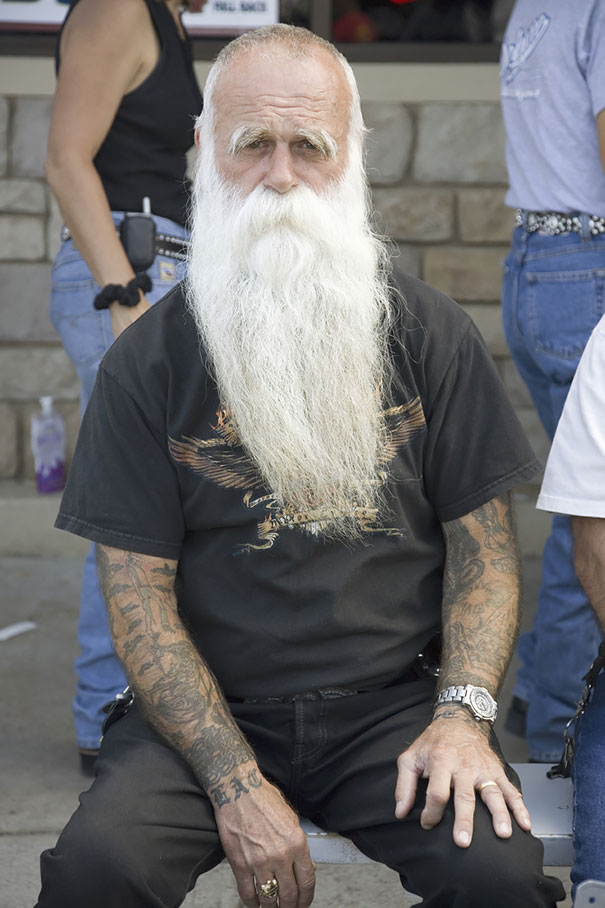 Senior man with tattoos and a long beard, wearing a black shirt, showcasing how ink looks in older age.