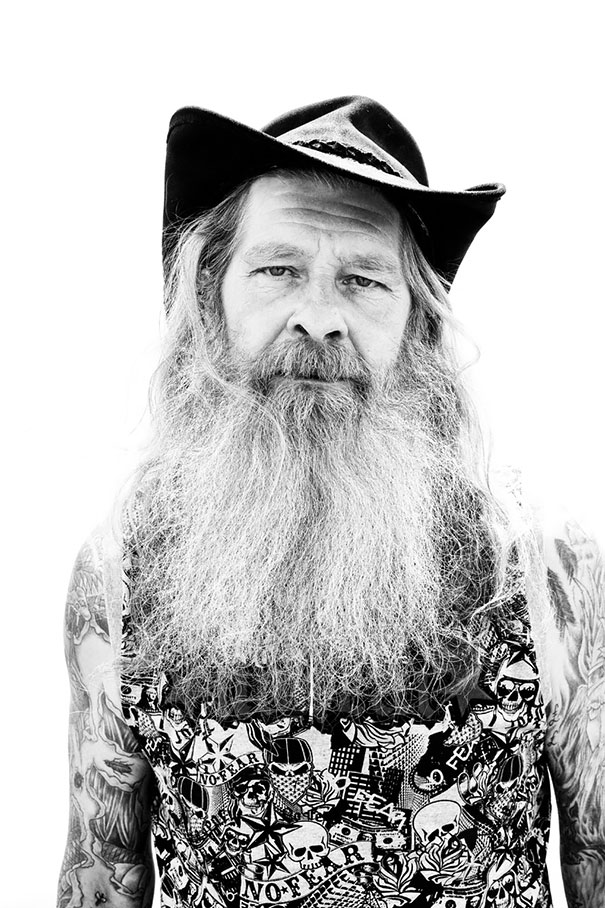 Senior man with tattoos and a long beard wearing a cowboy hat, showcasing aged ink.