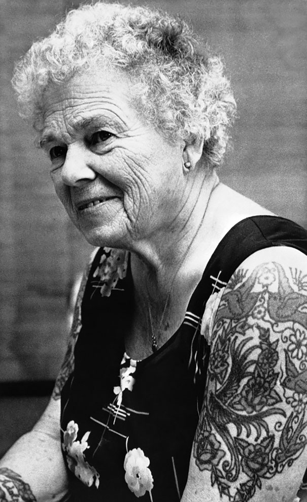 Senior woman with tattoos, smiling in a floral dress, showcasing how ink looks with age.