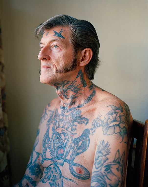 Tattooed senior man with detailed body art sits thoughtfully, illustrating how ink appears at 60.