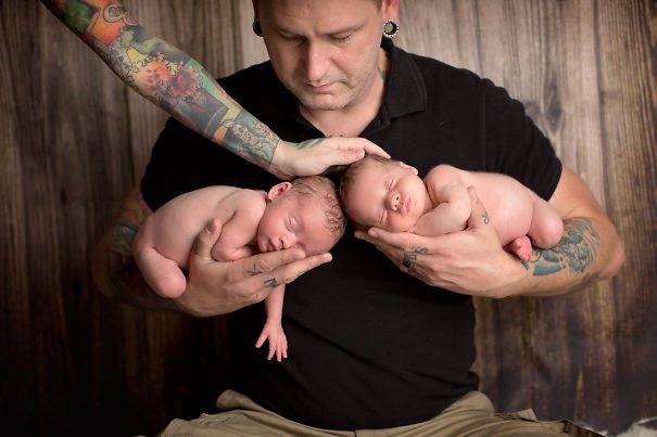 Tattooed parent tenderly holding twin babies, creating a beautiful moment together.