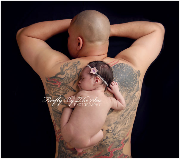Tattooed parent lying with baby on back, showcasing a detailed dragon tattoo.