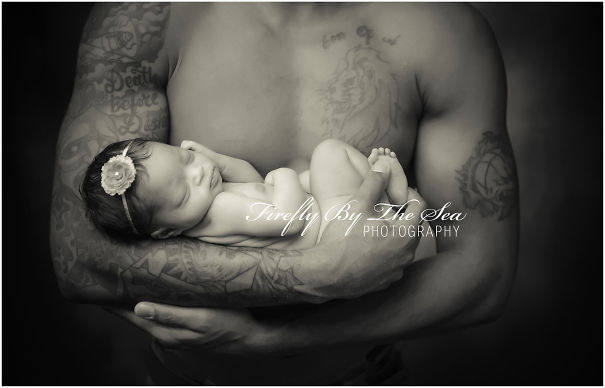 Tattooed parent cradling a sleeping baby adorned with a floral headband, showcasing a beautiful bond.