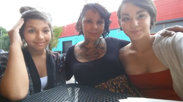 Tattooed parent with two children posing together outdoors, showcasing their beautiful family bond.