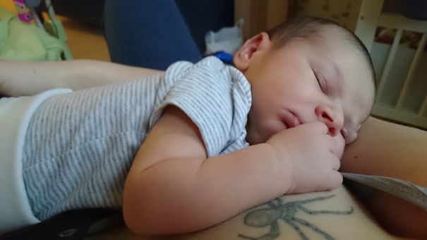 Baby sleeps on tattooed parent's arm, capturing a beautiful connection.