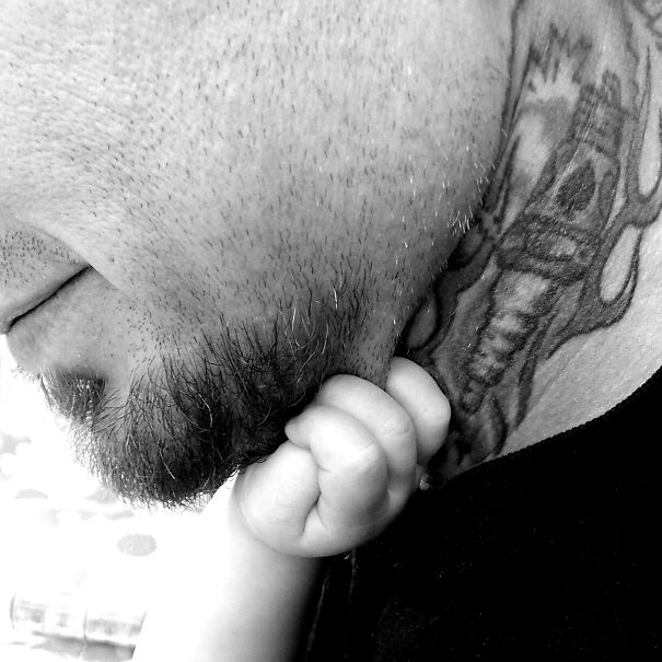 Baby's hand gently holding a tattooed parent's chin, showcasing a beautiful connection.