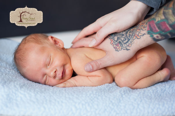 Tattooed parent gently touches their sleeping baby on a blue blanket, showcasing a beautiful family bond.