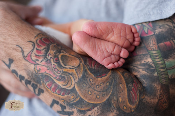 Tattooed parent cradling a baby's feet, highlighting the contrast between artful tattoos and delicate newborn skin.
