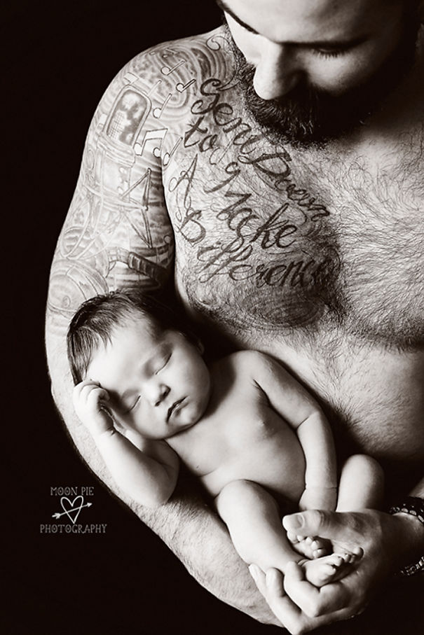 Tattooed parent cradles sleeping baby, displaying tender bond and intricate body art.