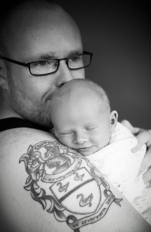 Tattooed parent gently holding smiling baby, showcasing beautiful bond together.