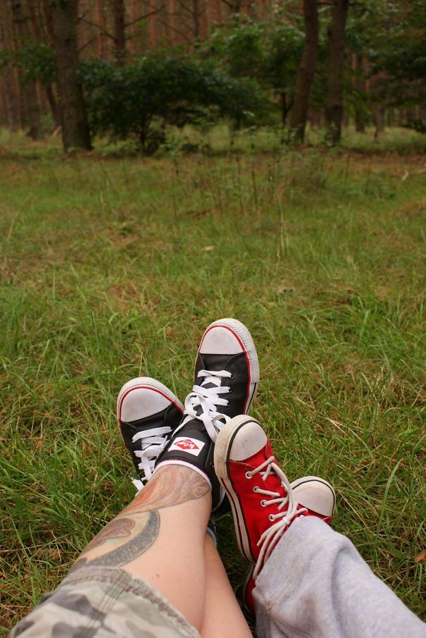 Tattooed parent and child wearing sneakers relaxing on grass in the forest.