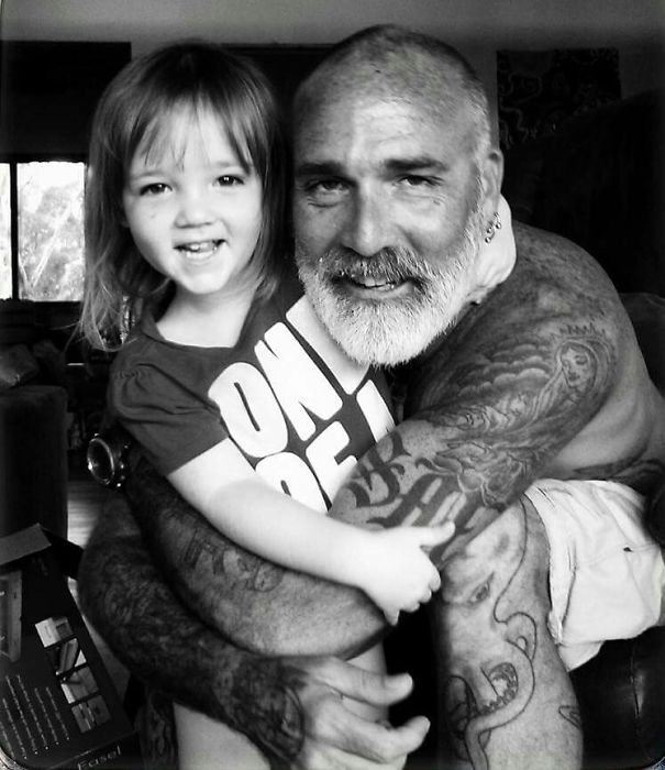 Tattooed parent hugging smiling baby, showcasing beautiful bond.