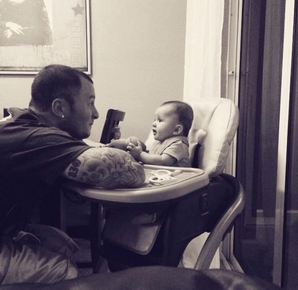 Tattooed parent joyfully interacting with their baby in a high chair, showcasing a beautiful family connection.
