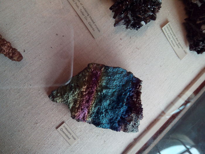 Iridescent mineral stone with vibrant colors displayed on a beige surface with label.