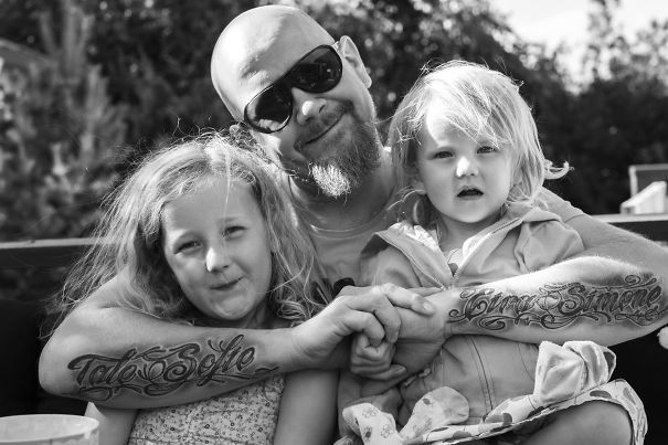 Tattooed parent with two young children, enjoying time together outdoors.