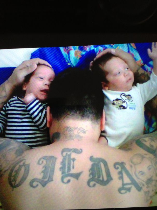 Tattooed parent with twin babies, lying together on a colorful blanket.