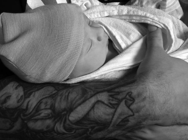 Baby wrapped in a blanket, held by a tattooed parent, showcasing beautiful art and bond together.