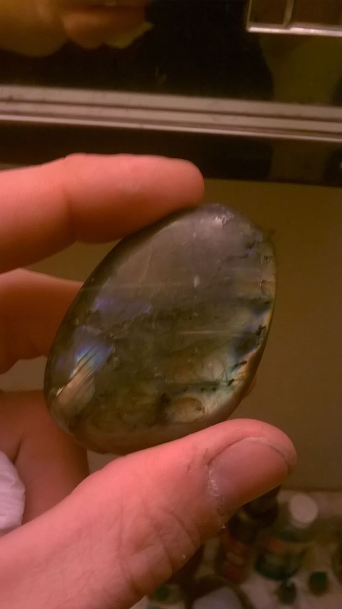 Person holding a beautiful mineral stone with iridescent colors reflecting light.