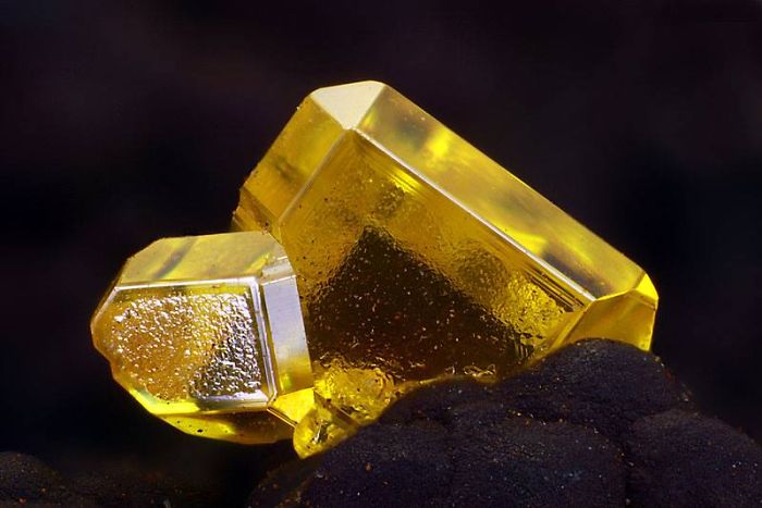 Bright yellow mineral stone with geometric shapes, glowing against a dark background.