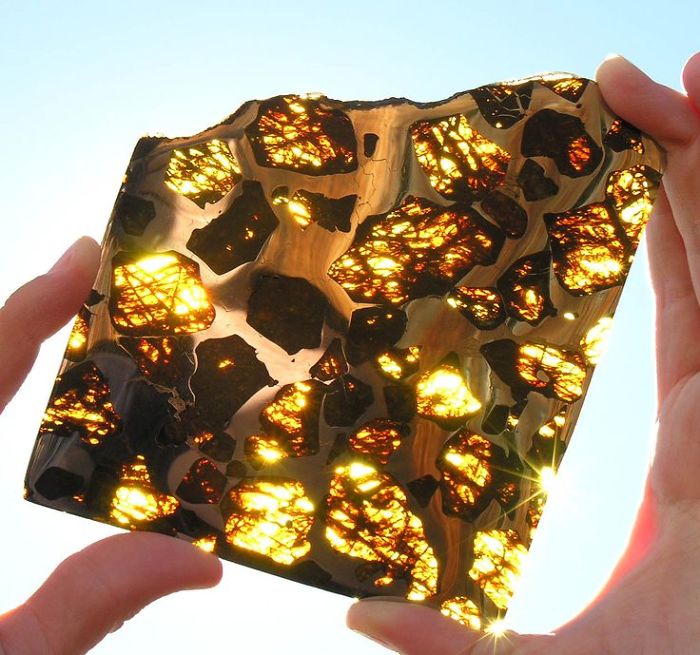 Hands holding a beautiful mineral slice with golden hues against the sky.