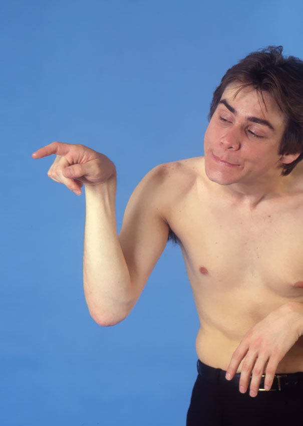 Jim Carrey shirtless against blue background, making a dramatic hand gesture in manic celeb impressions from 1992.