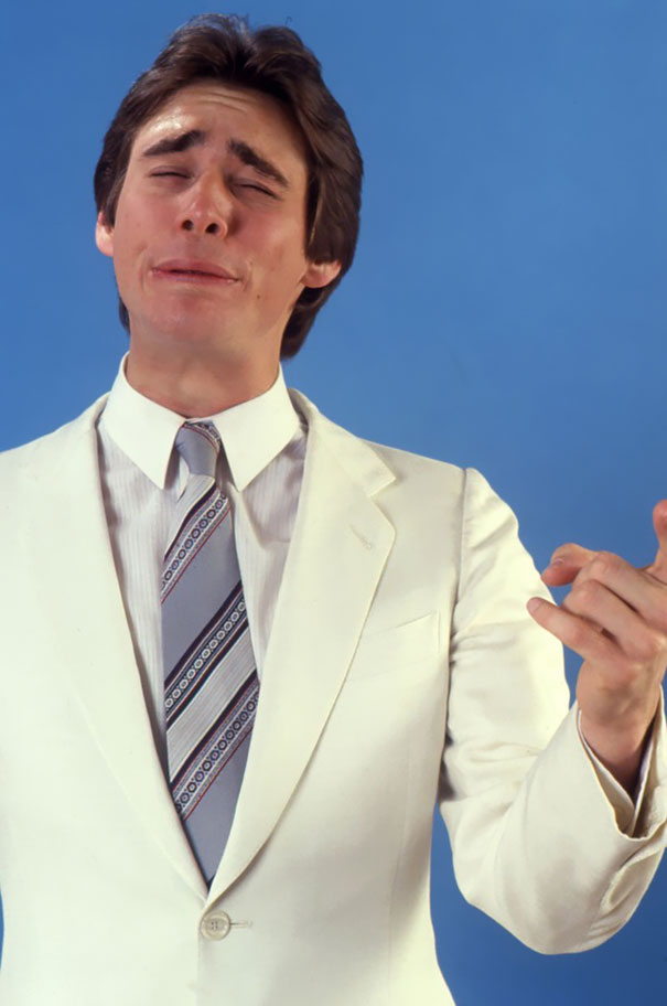Young Jim Carrey in a white suit performing manic celeb impressions with an expressive face against a blue background. Young Jim Carrey in a white suit performing manic celeb impressions with an expressive face against a blue background.