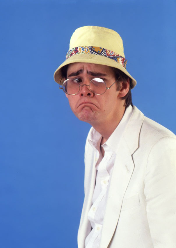 Young Jim Carrey in 1992 wearing glasses and a yellow hat, making a comical expression during manic celeb impressions.