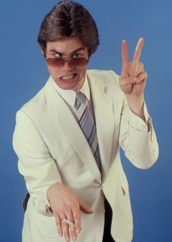 Young Jim Carrey in a white suit and sunglasses making a manic pose for celeb impressions in 1992.