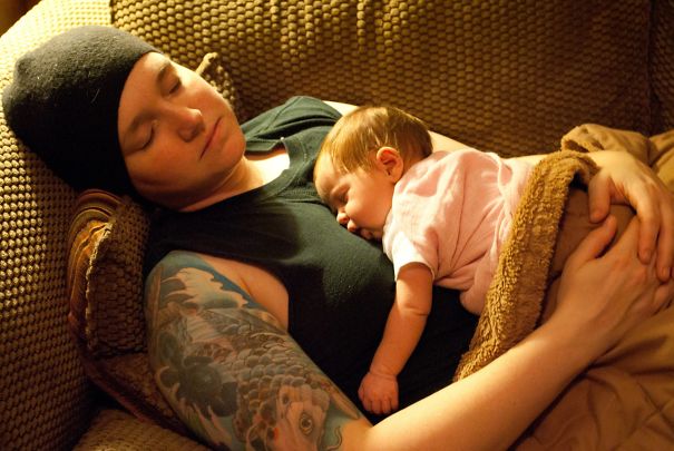 Tattooed parent and baby sleeping together on a couch, showcasing a beautiful bond.