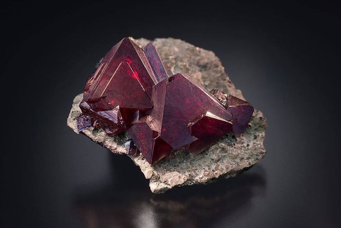Deep red minerals with sharp edges on a stone surface, showcasing beautiful mineral formations.