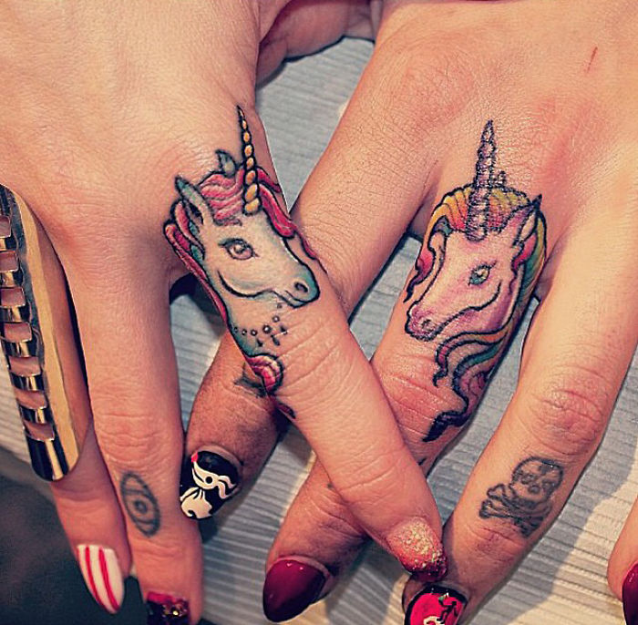 Unicorn finger tattoos on crossed hands with colorful nail art.