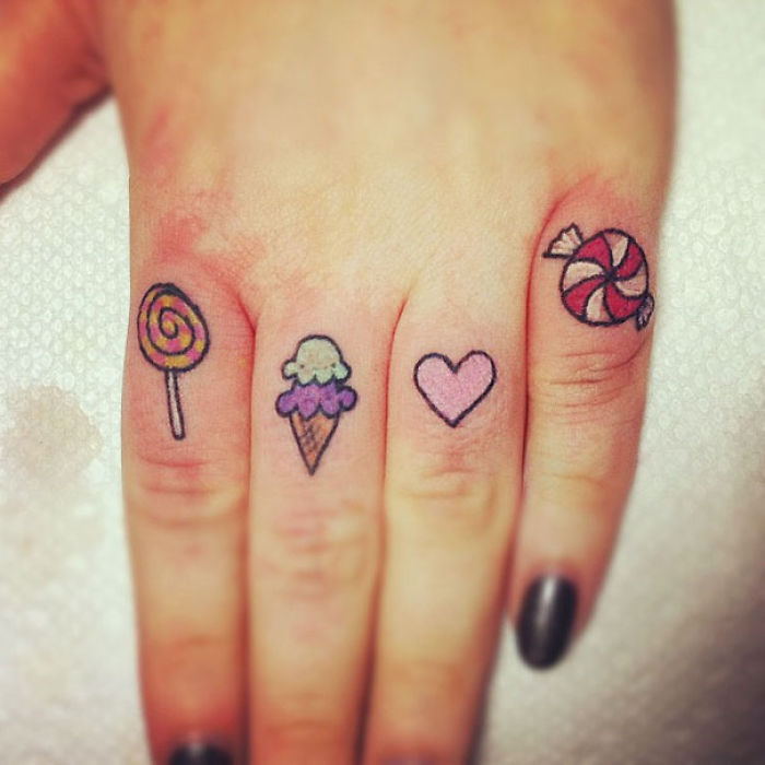 Colorful finger tattoos of candy and heart designs on a hand.