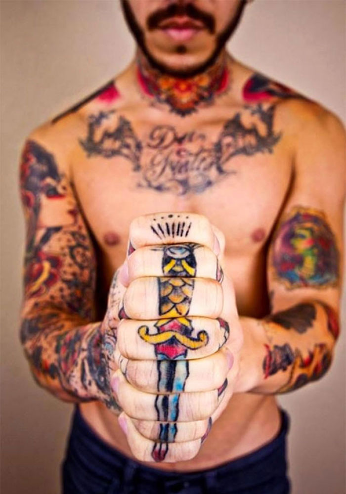Man with colorful finger tattoos and body art, featuring an intricate design on his fists.