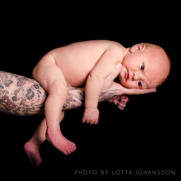 Tattooed parent holding a baby gently in their arms against a dark background.