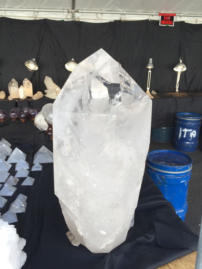 Large, transparent quartz crystal displayed among various beautiful minerals and stones.